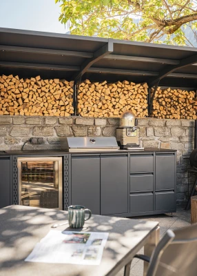 Outdoorküche mit Grillstation und Holzlager unter einem modernen Schutzdach.